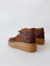Zapatillas acordonadas de cuero marrón con detalles en rojo y suela de goma color caramelo.