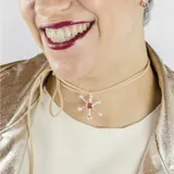 Gargantilla con dije de plata 950 en forma de sol con piedra roja en el centro, atada con tiento color beige.