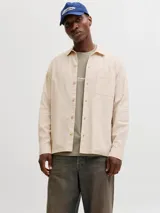 Sobrecamisa de manga larga color beige claro, con cierre frontal de botones, cuello camisero y un bolsillo aplicado en el pecho.