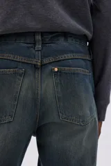 Jean de cinco bolsillos en denim de algodón rígido, color azul oscuro con efecto desgastado y lavado. Corte de tiro alto con pierna acampanada amplia.