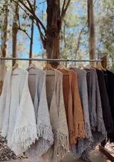 Ruana tejida a mano en lana merino, con diseño en V y terminación de flecos en el ruedo. Presenta una textura gruesa y una caída envolvente.