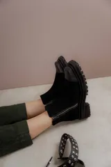 Bota corta de cuero gamuzado color marrón chocolate, con punta cuadrada y suela track. Presenta una correa con hebilla desmontable y cierre lateral con cremallera.