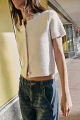 Chaqueta de punto de lana con manga corta, cuello redondo decorado con abalorios joya y cierre frontal con botones forrados a tono.