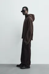 Sudadera de corte boxy fit en color marrón oscuro, con capucha, mangas largas y bandas laterales a contraste. Presenta un diseño de bajo con acabado irregular deshilachado.