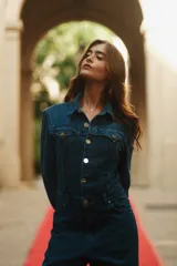 Mono de denim azul con cierre frontal de botones metálicos, cuello camisero, mangas largas y bolsillos delanteros.