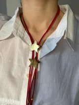 Corbatín rojo de gamuza con dos dijes de estrella dorada.