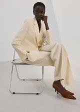 Blazer de diseño recto y estilo sastrero, color beige, confeccionado en mezcla de lyocell y poliéster. Cuenta con cuello en pico con solapas de muesca, manga larga, bolsillos delanteros con solapa y cierre frontal de un botón.