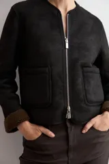 Chaqueta reversible de corte recto con cierre frontal de cremallera. Presenta un lado en acabado de gamuza negra y el reverso en tejido de textura tipo corderito color marrón chocolate, con cuello redondo y bolsillos frontales.