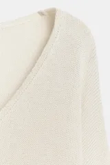Jersey de punto de color blanco crudo, con escote en V y mangas largas con sisas amplias y puños elásticos acanalados.