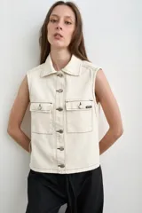 Chaleco de denim crudo de corte recto, con cuello camisero, sin mangas y cierre frontal con botones metálicos. Cuenta con dos bolsillos delanteros con solapa y costuras pespunteadas en contraste.