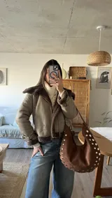 Campera tipo gamulán de cuero sintético en color vizón, con interior y solapas de piel sintética en color marrón oscuro. Presenta cierre frontal, correas ajustables con hebillas en los puños y diseño de corte recto.