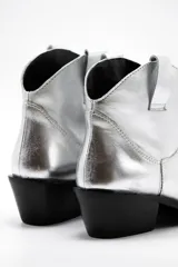 Botas de cuero vacuno color negro con caña baja bordada a tono, tacón bajo, punta alargada redondeada y suela cuadrada.