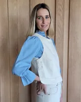 Chaleco de corte recto y largo a la cintura, confeccionado en denim con estampado de rayas verticales en tonos azul y blanco. Presenta cuello redondo y costuras visibles que definen su estructura.