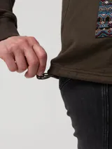 Buzo tipo campera de algodón orgánico color verde militar, con cierre frontal de botones a presión, capucha forrada con estampado étnico y bolsillos frontales con detalles de tejido aguayo multicolor.