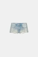 Shorts de denim de tiro medio con cinco bolsillos, detalles de rotos y aplicación de tachas metálicas en la parte delantera. El bajo presenta un acabado deshilachado sin costuras.