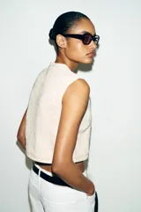 Chaleco de punto color crudo con textura estructurada, cuello redondo y cierre frontal con botones negros a contraste.