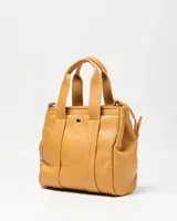 Cartera mediana de símil cuero color habano, con doble asa corta de mano y correa ajustable extraíble. Cuenta con un bolsillo frontal con broche a presión, herrajes metálicos plateados y un llavero colgante en forma de corazón.
