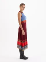 Vestido midi de punto sin mangas con diseño plisado. Presenta un corte evasé con rayas horizontales en tonos rojo, rosa y negro en el cuello, la cintura y el ruedo, el cual cuenta con terminaciones irregulares y detalles de transparencia.