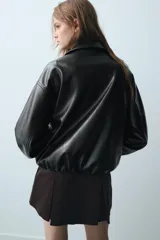 Cazadora de efecto piel en color negro, con cuello solapa, cierre frontal de cremallera metálica, bolsillos laterales de vivo y mangas largas con puños elásticos.