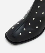 Bota de caña corta confeccionada en poliuretano color negro, con punta cuadrada, taco bloque y aplicación de studs metálicos en toda la superficie. Cuenta con cierre lateral.