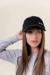 Gorra de gamuza negra con visera curva y aplique metálico decorativo con la marca en el lateral frontal.
