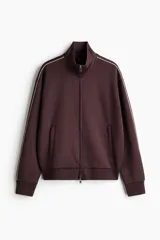 Campera deportiva de cuello elevado con cierre frontal, hombros caídos y ribetes en contraste a lo largo de las mangas. Presenta bolsillos laterales y puños con terminación acanalada.