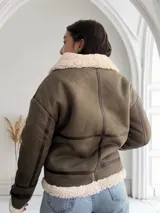 Chaqueta gamulan color verde con interior de piel sintética blanca, cierre frontal con cremallera y detalles en cuero marrón.