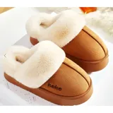 Pantuflas de gamuza color tostado con interior de corderito sintético color crema. Presentan diseño sin talón, plataforma plana y detalle de marca bordada en el lateral.