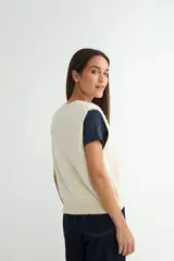 Chaleco de punto color crema con escote en V, sin mangas y diseño decorado con pequeñas perlas aplicadas en toda la superficie.