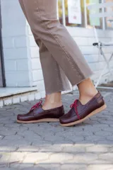 Zapato náutico de cuero color marrón con cordones rojos y suela color caramelo.