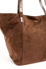 Bolso tipo tote bag color marrón, confeccionado en gamuza vegana con detalles de tiras y asas de hombro en cuero sintético brillante. Incluye una placa metálica pequeña con el logo de la marca en el frente.
