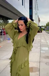 Vestido midi de gasa color verde oliva, con escote en V, mangas largas con puños elásticos y detalle de volados en la falda con abertura lateral.