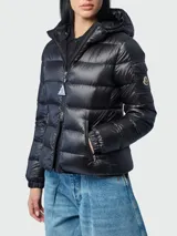 Campera puffer Moncler modelo Glesse, color negro, con diseño acolchado horizontal, capucha ajustable, cierre frontal y bolsillos laterales con cierre. Cuenta con un bolsillo con solapa y parche del logo en la manga izquierda.