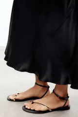 Sandalias planas negras con tira dorada en la parte delantera y tira con hebilla en el tobillo.