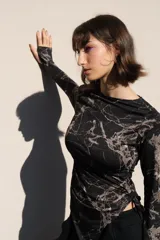Top de manga larga color negro, confeccionado en jersey elástico. Presenta un diseño asimétrico con jaretas laterales regulables que permiten ajustar el largo y el volumen, y aberturas para los pulgares en los puños.