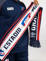 Bufanda tejida del Club Nacional de Football, con diseño tricolor en blanco, azul y rojo. Presenta inscripciones con letras grandes y el logo de Umbro en los extremos, finalizando con flecos decorativos.