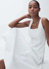 Vestido midi de algodón blanco con diseño evasé, cuello cuadrado y tirantes anchos. Presenta un tejido bordado con detalles calados y costuras horizontales que crean un efecto de paneles.