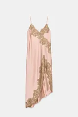 Vestido largo tipo lencero de satén color rosado, con escote en pico y tirantes finos. Presenta aplicaciones de encaje a contraste en el escote y en el lateral, con un diseño de bajo asimétrico.