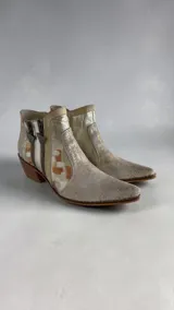 Bota de caña corta de cuero en tonos natural y dorado light, con diseño pintado a mano y puntera fina. Cuenta con taco bloque de madera y doble cierre lateral con tiradores personalizados.