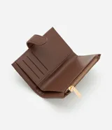 Billetera femenina pequeña de material sintético color marrón, con textura grabada y cierre de cremallera con solapa con broche a presión.