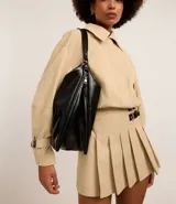 Cartera tipo hobo de gran tamaño confeccionada en poliuretano color negro, con acabado liso y brillante. Presenta un diseño de media luna con cierre superior de cremallera, correa de mano fija y asa larga desmontable. Incluye un detalle de cremallera lateral que permite expandir su capacidad interna.