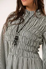 Vestido largo a rayas verticales en tonos verde y blanco, con cuello alto fruncido, mangas largas abullonadas y falda amplia. Presenta un diseño de nido de abeja con hilo elástico hasta la cintura.