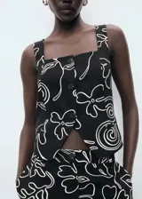 Top de mezcla de lino y viscosa, sin mangas, con tirantes anchos, escote cuadrado y cierre frontal de tres botones. Presenta un estampado lineal de flores blancas sobre fondo negro.