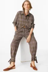 Pantalón de tiro medio con estampado a cuadros, corte holgado y pinzas en la cintura. Presenta un diseño distintivo con tiras ajustables en los tobillos que permiten crear un efecto fruncido.