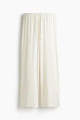 Pantalón de pijama color crema en punto pointelle, con piernas levemente acampanadas. Tiene cintura elástica revestida, ribete de volados y cordón fino para ajustar.