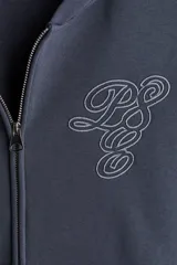 Campera con capucha de algodón pesado, color azul oscuro o gris pizarra, con cierre frontal bidireccional y bolsillos canguro. Presenta un corte holgado (boxy) con hombros caídos y puños y bajo acanalados.