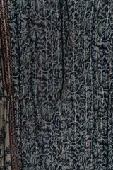 Vestido corto con estampado floral en tonos azul oscuro y beige, con detalles en hilo metalizado. Presenta escote pico con cordón ajustable terminado en borlas, mangas largas acampanadas y cintura elástica ajustable.