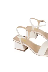 Sandalias de cuero color crudo, con tira ancha sobre el empeine, pulsera fina ajustable al tobillo y tacón bloque de aproximadamente 5 cm.