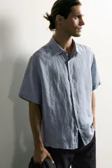 Camisa regular fit confeccionada en tejido de lino, color blanco, con cuello solapa, manga corta y cierre frontal de botonadura.