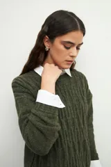 Sweater de tejido tramado en color verde oliva, con cuello redondo y mangas largas. Presenta un diseño de textura acanalada vertical.